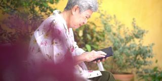 亚洲老人老年人老年人妇女老年人男性使用手机智能手机户外。成熟的退休生活