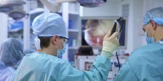 医疗团队背景上的大监视器。在现代化的手术室里，由专业的外科医生和助手进行外科手术。医生在医院外科手术中使用现代医疗设备。