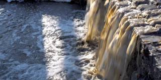 在一个阳光明媚的日子里，肮脏的浑水像瀑布一样从下水道流入河里。特写镜头。环境污染的概念。4 k。