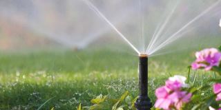 塑料洒水车在夏季花园用水灌溉草坪。在旱季灌溉绿色植被，保持其新鲜