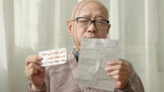一位中国老人坐在窗边，戴着老花镜，阅读说明书视频素材模板下载