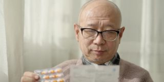 一位中国老人坐在窗边，戴着老花镜，阅读说明书