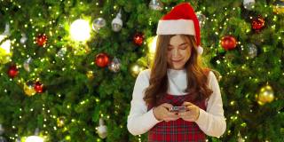 快乐女人用智能手机与圣诞树，欢度圣诞