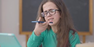 千禧一代的智能小人坐在大学教室里用智能手机扬声器说话。戴着眼镜的年轻白人妇女在室内录音的肖像。