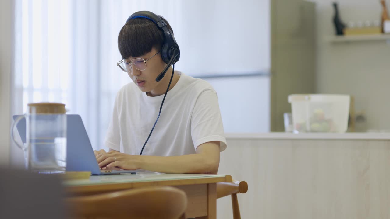 年轻的亚洲商人使用笔记本电脑与同事在视频电话中谈论计划，而聪明的在家工作在客厅。