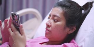亚洲病人妇女使用触摸屏智能手机设备在医院的床上。