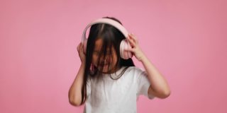 日本女孩戴着耳机听音乐跳舞在粉红色的背景
