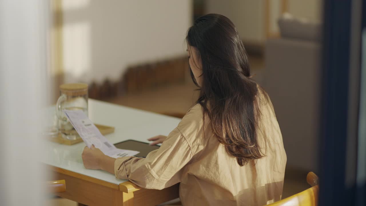 年轻的亚洲妇女在家里的桌子上用计算器计算财务家庭，检查账单，为家庭节省开支成功