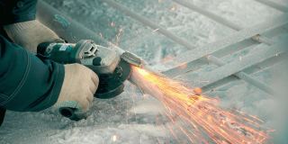 冬季工人用角磨机处理金属门，火花飞舞。特写的慢动作视频