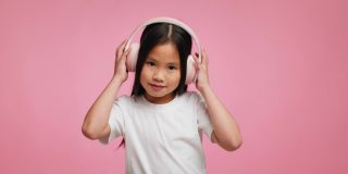 韩国小女孩戴着耳机听音乐在粉红色的背景
