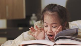 近距离4K的可爱的5岁亚洲女孩，她正在床上看书，美丽的黄色灯光从一盏灯。就寝时间是孩子学习、放松和发展创造力的时间。视频素材模板下载