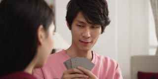 狡猾的亚洲儿子在淡红色试图影响他的妹妹与滑稽的脸和感觉不安，因为她选了一张好牌。春节假期和家人在家里打扑克