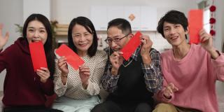 快乐的亚洲父亲，母亲，女儿和儿子在镜头前微笑，炫耀他们手中的红包，并与朋友在中国新年视频电话