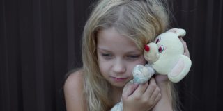 一个不整洁的女孩脸上的表情，手里拿着一个简单的玩具。蓬乱的头发和孩子的悲伤表情。