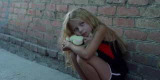 一个孤独，害怕的女孩的肖像，美丽的凌乱的头发坐着，她的玩具靠着砖墙。