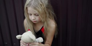 一个不整洁的女孩脸上的表情，手里拿着一个简单的玩具。蓬乱的头发和孩子的悲伤表情。