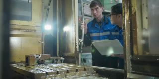 种族多样性工厂技术员工程师制造工业，白人和亚洲工业工程师咨询讨论，以提高质量的加工和自动螺纹操作的一个工程零件在数控铣床设置过程。
