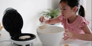 年轻的混合亚洲女孩帮助在家里做华夫饼的早餐，家庭教育，蒙特梭利教育的概念