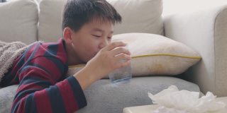 生病的十几岁男孩在沙发上喝水和休息，保健概念