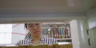 亚洲女孩在图书馆的书架上寻找书。