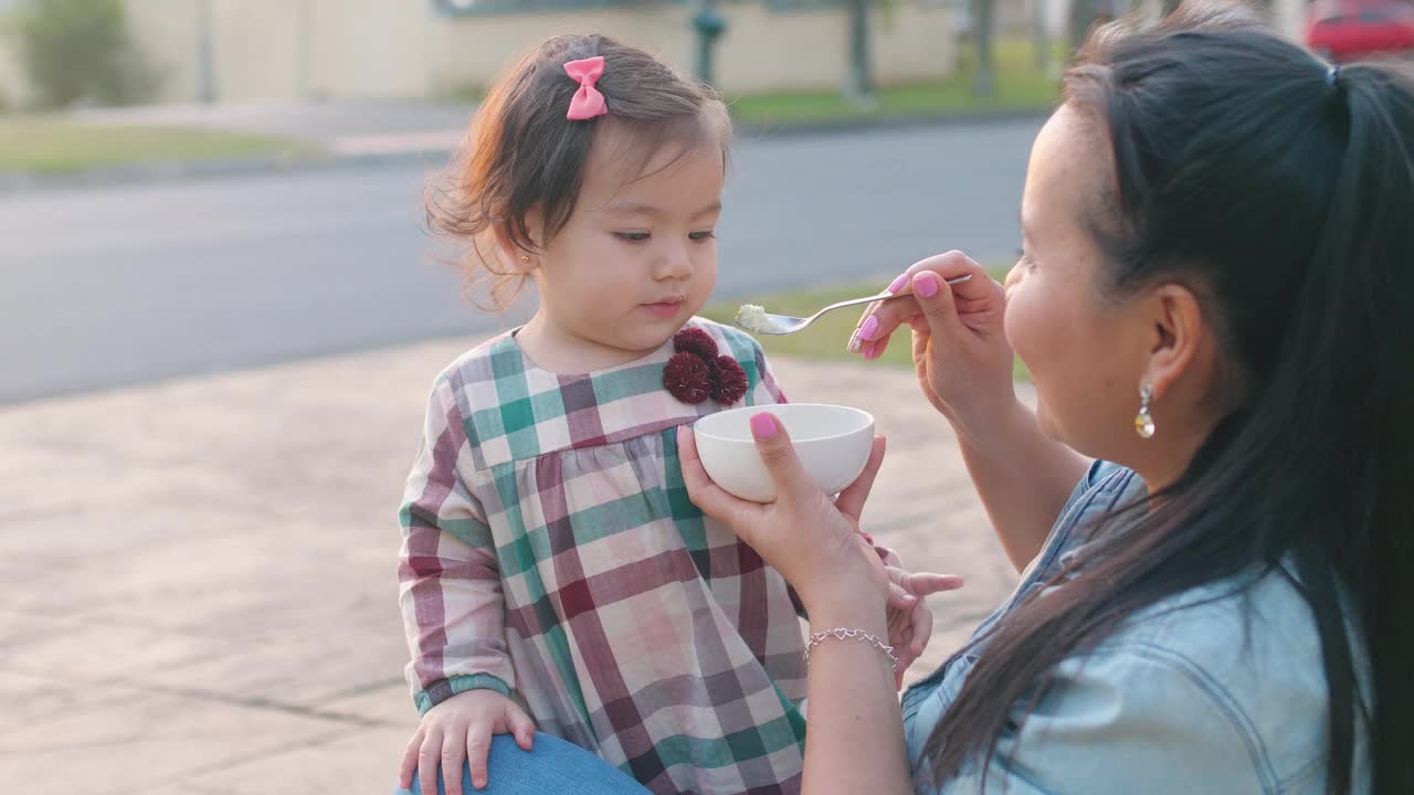 亚洲母亲在前院喂养她的混合蹒跚学步的女儿，家庭生活理念