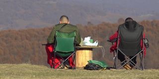 两名认不出的男子在山上野餐，欣赏秋天五彩山的景色