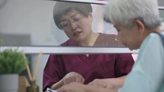 亚裔华人老年女性在诊所用信用卡支付医疗费用，由女护士手持信用卡读卡器视频素材模板下载