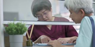 亚裔华人老年女性在诊所用信用卡支付医疗费用，由女护士手持信用卡读卡器