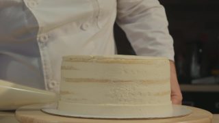 穿着白色衣服的糕点师创造了蛋糕的形状。他把奶油从冷却器里压到蛋糕的边缘。甜点视频素材模板下载