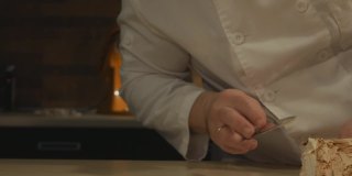 糖果师夫妇在糕点店工作。一名男子将奶油涂在蛋白酥皮卷上，背景中的一名女子用餐巾擦桌子，以保持清洁