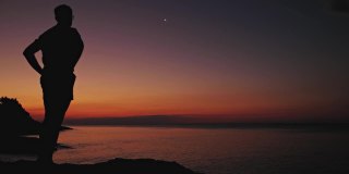 一个人的剪影看着月亮和星星在海上的地平线。