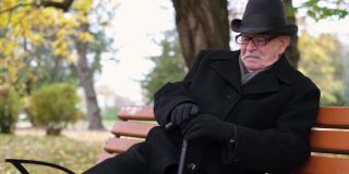 秋天的城市公园里，孤独的老爷爷拿着一根棍子坐在长椅上。