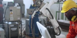 多种族的工程师在工厂工作，用电脑和平板检查焊接机器人手臂。经理工程师检查和控制仓库自动化机器人手臂机器
