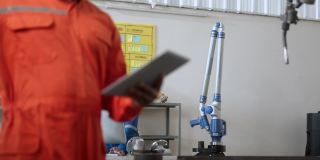 多种族的工程师在工厂工作，用电脑和平板检查焊接机器人手臂。经理工程师检查和控制仓库自动化机器人手臂机器