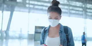 年轻的亚洲女性休闲布手出示护照和机票在工作人员的航空服务台办理旅行假期登记，安全旅行的亚洲女性带着口罩在机场候机楼办理登机手续