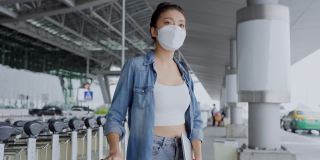 迷人的亚洲女性穿着休闲旅游服饰，戴着口罩保护行走在候机候机大楼的户外背景下，亚洲女性的旅游理念
