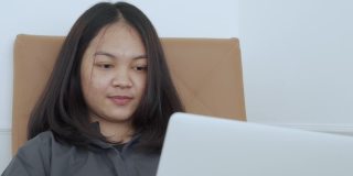 4k, Portrait，一个可爱的亚洲少女。穿着灰色衬衫坐在椅子上，带着笔记本电脑在卧室里开心地上网学习