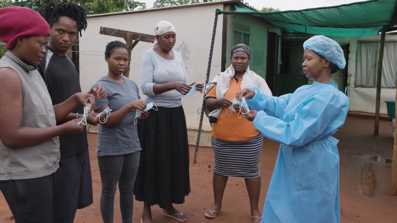 非洲黑人女护士向农村居民点的人们演示如何戴上防护口罩，以预防Covid-19