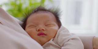 可爱的睡着的新生儿在妈妈的臂弯里放松，安全舒适。微笑亚洲新生儿婴儿休息睡眠甜蜜的梦。母亲抱着婴儿。新生儿摄影理念
