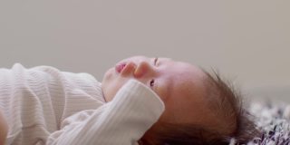 侧视图快乐的新生儿躺在地毯上看着相机，微笑舒适和安全。幸福可爱的亚洲新生儿在地毯上睡觉和打盹。新生儿摄影理念