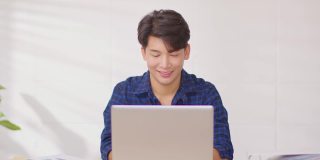 企业家英俊的商人亚洲人穿蓝色衬衫完成工作，在网上关闭电脑笔记本电脑桌上桌子微笑和幸福。有吸引力的自由职业者在线销售营销在家里的办公室