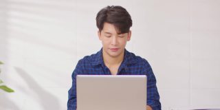 企业家英俊的商业亚洲男人穿着蓝色衬衫在笔记本电脑桌上工作，接听手机与客户交谈，以获得要求或订单微笑和快乐的工作在家里