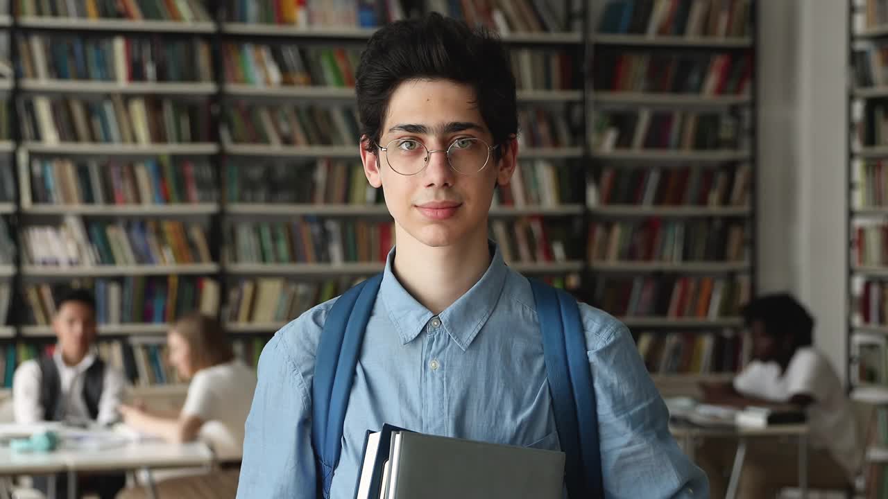 一个拿着课本的16岁高中生在图书馆摆姿势