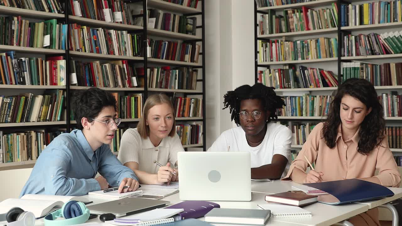 4名来自不同民族的学生带着笔记本电脑坐在图书馆里学习