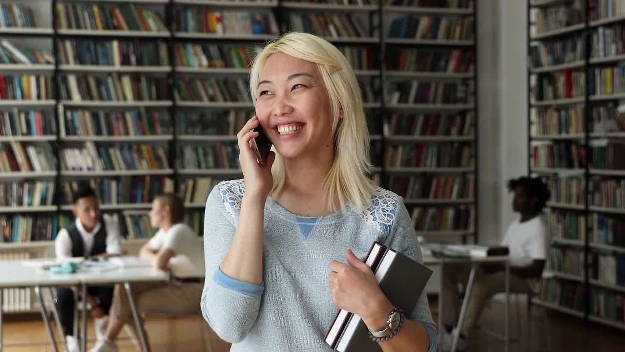 有吸引力的亚洲女学生站在图书馆闲谈电话