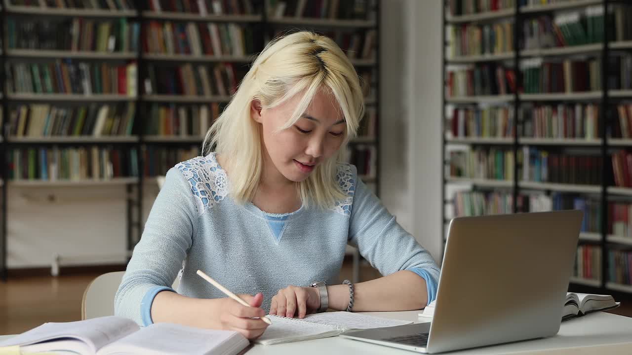 亚洲学生坐在桌旁用笔记本电脑写论文