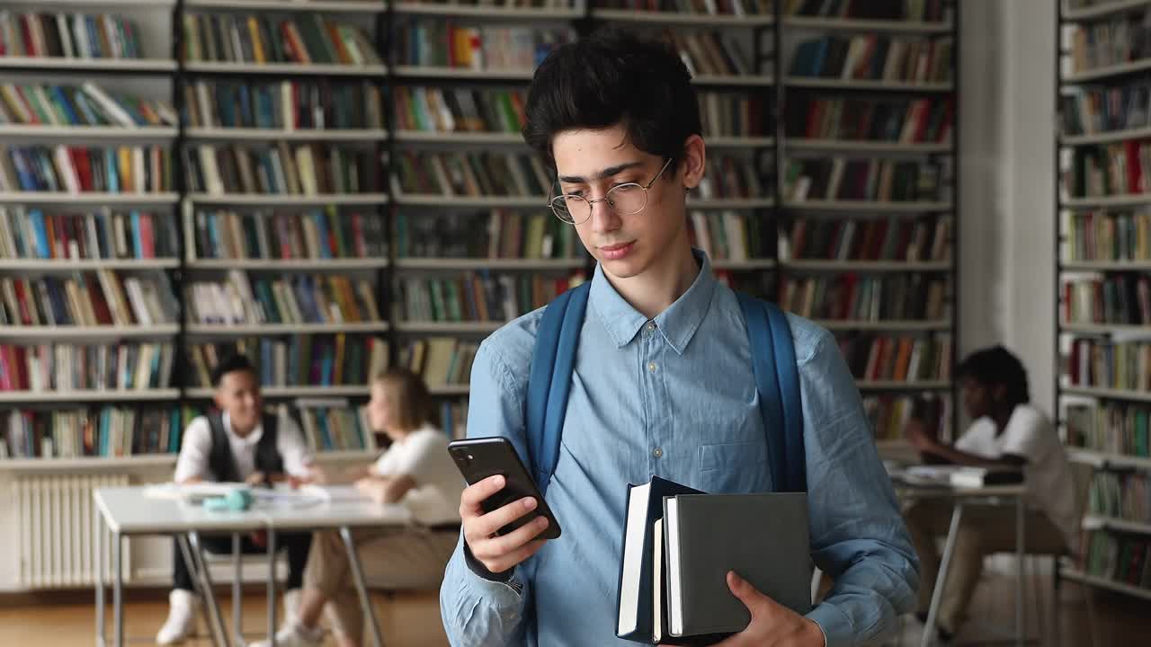 一名学生站在大学图书馆里拿着手机查看短信