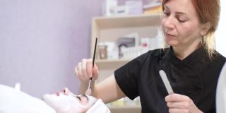 美容师在美容诊所、水疗沙龙用化妆刷给年轻漂亮的女性脸上涂面膜