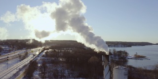 在一个阳光明媚的冬日里，瑞典斯堪的那维亚，发电厂的烟囱里飘着污染的烟雾，以火车和高速公路为背景发电