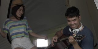 情侣们，在帐篷里度过快乐的一天，男人在度假时弹吉他。